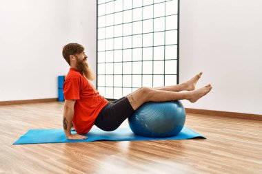 Genç kızıl saçlı, gülümseyen, kendine güvenen bir adam spor merkezinde formda top kullanıyor.