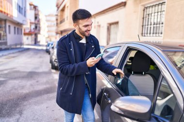 Young hispanic man using smartphone leaning on car at street