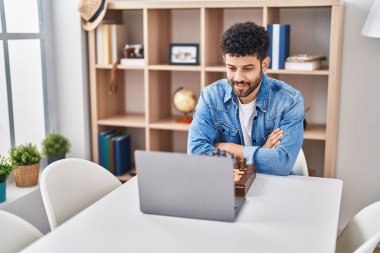 Genç Arap adam evdeki masada online satranç oynuyor.