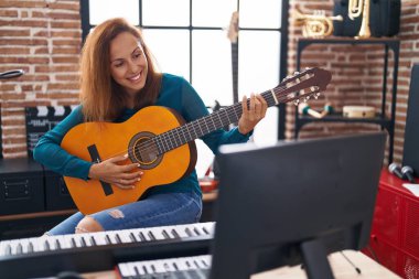 Young woman musician playing classical guitar at music studio