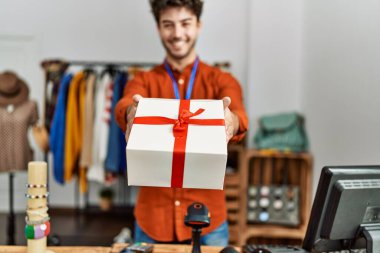 Genç İspanyol esnaf gülümseyerek giyim mağazasında hediyesini tutuyor..