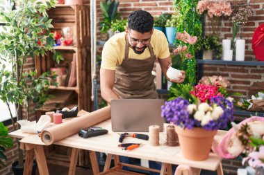 Young arab man florist using laptop holding plant at florist