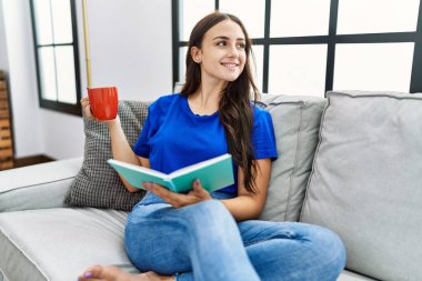 Beyaz bir kadın gülümseyerek evde kahve içiyor.