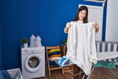 Genç, güzel, İspanyol bir kadın çamaşırhanede giysileri ütülüyor.