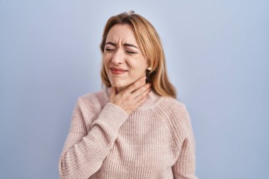 Hispanic woman standing over blue background touching painful neck, sore throat for flu, clod and infection 