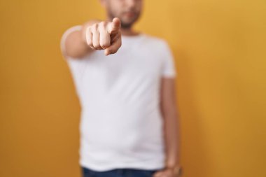 Sarı arka planda beyaz tişörtlü İspanyol bir adam kamerayı işaret ediyor ve sen kendine güvenen ciddi bir hareket yapıyorsun. 