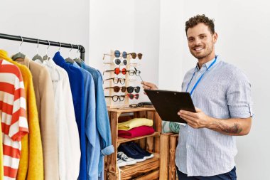 Genç İspanyol esnaf gülümseyerek giyim mağazasında çalışan mutlu bir pano tutuyor..