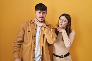 Young hispanic couple standing over yellow background cutting throat with hand as knife, threaten aggression with furious violence 