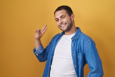 Sarı arka planda dikilen İspanyol adam kameraya bakıp zafer işareti yapıyor. İki numara.. 