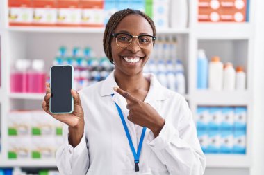 Eczanede çalışan Afro-Amerikalı kadın akıllı telefon ekranı göstererek mutlu bir şekilde el ve parmak işareti yapıyor. 