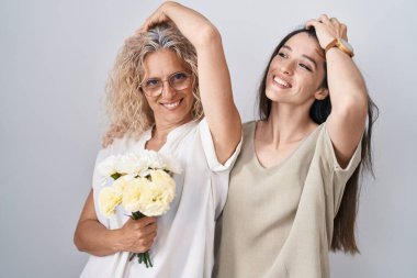 Anne ve kızı ellerinde bir buket beyaz çiçekle gülümseyerek saçlarına dokunarak el hareketleriyle çekici ve modaya uygun bir poz veriyorlar. 