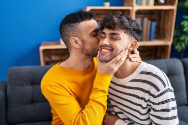 İki erkek birbirine sarılıyor ve evdeki koltukta öpüşüyorlar.