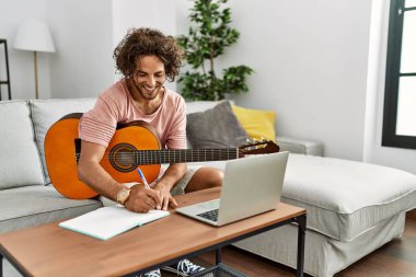 Genç İspanyol besteci evde gitar ve dizüstü bilgisayar kullanarak beste yapıyor..