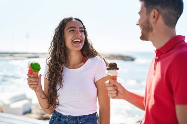 Young hispanic couple tourists eating ice cream at seaside