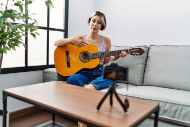 Beyaz bir kız evdeki koltukta kamerayla gitar konseri kaydediyor..