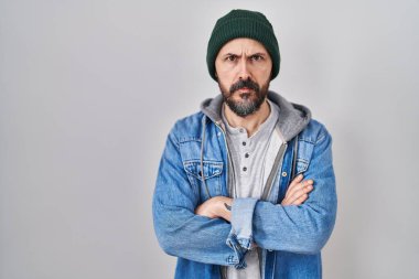 Yün kapşonlu, kuşkucu ve gergin dövmeli genç İspanyol bir adam. Yüzünde çapraz kollarla onaylamayan bir ifade var. negatif kişi. 