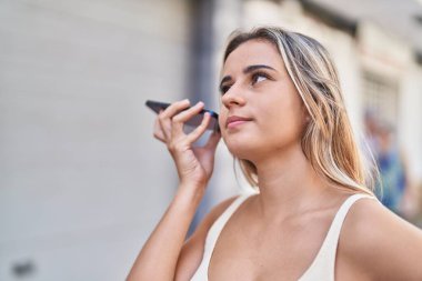 Akıllı telefondan sesli mesaj dinleyen genç sarışın kadın. Sokakta ciddi bir ifadesi var.