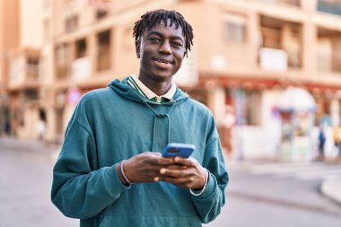 Sokakta akıllı telefon kullanan, kendinden emin gülümseyen Afrikalı Amerikalı bir adam.