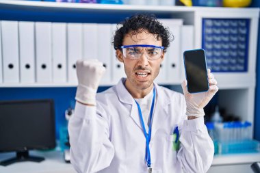 Laboratuvarda çalışan İspanyol bir adam akıllı telefon ekranında öfkeyle bağırıyor, öfkeyle bağırıyor ve el kaldırıyor. 