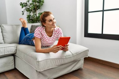 Evdeki kanepede uzanmış dokunmatik ped kullanan genç bir kadın.