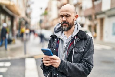 Genç kel adam akıllı telefon kullanıyor ve sokakta ciddi bir yüz ifadesi var.