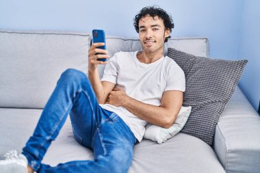 Evdeki kanepede oturan, akıllı telefon kullanan genç bir İspanyol.