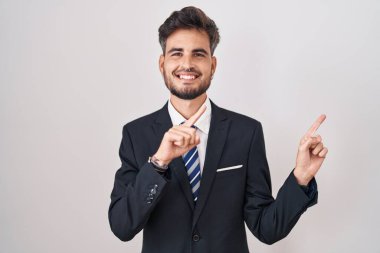 Dövmeli, takım elbiseli, kravatlı, gülümseyen ve kameraya bakan iki eli ve parmakları yanda olan genç İspanyol bir adam.. 