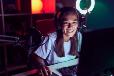 Young beautiful hispanic woman streamer playing video game using computer at gaming room