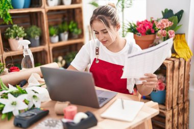 Young blonde woman florist using laptop reading document at flower shop