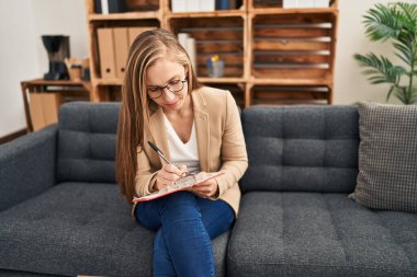 Psikoloji kliniğinde genç sarışın kadın psikolog belgeye yazı yazıyor.