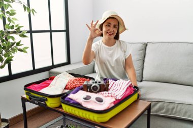 Güzel orta yaşlı İspanyol kadın valize yazlık giysiler yerleştiriyor gülümsüyor ve el ve parmaklarıyla 