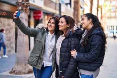 Three woman mother and daughters make selfie by the smartphone at street