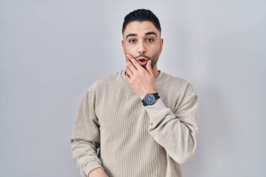 Tecrit edilmiş arka planda duran yakışıklı genç adam elleri çenesinde, inanamama, şaşkınlık ve şaşkınlık dolu bir ifade takınıyor. 