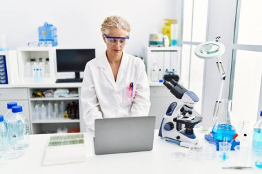 Laboratuarda çalışan orta yaşlı sarışın kadın bilim adamı üniforması giyiyor.