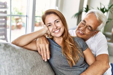 Orta yaşlı İspanyol çift mutlu bir şekilde gülümsüyor ve evdeki kanepede oturup sarılıyorlar..