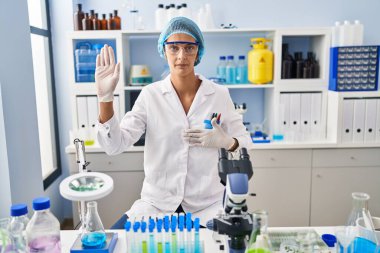 Brunette woman working at scientist laboratory swearing with hand on chest and open palm, making a loyalty promise oath 