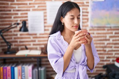 Young beautiful hispanic woman smiling confident smelling coffee at home