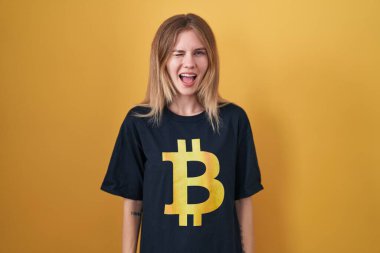 Bitcoin tişört giyen sarışın beyaz kadın kameraya seksi bir ifadeyle bakıyor, neşeli ve mutlu bir yüz.. 