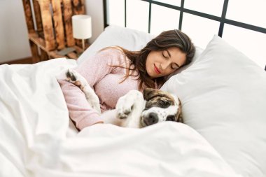 Genç bir kadın yatak odasında bir köpekle yatakta uyuyor.