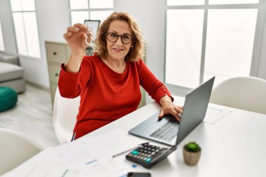 Middle age caucasian woman holding key of new home working at the office.