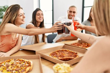 Group of young friends smiling happy eating italian pizza and toasting with cola beverage at home.