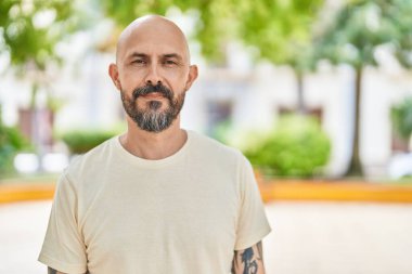 Genç kel adam parkta kendine güvenerek gülümsüyor.