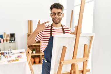 Sanat stüdyosunda gülümseyen, neşeli gülümseyen ve parmaklarıyla ve ağzıyla işaret eden Arap genç bir adam. diş sağlığı kavramı. 