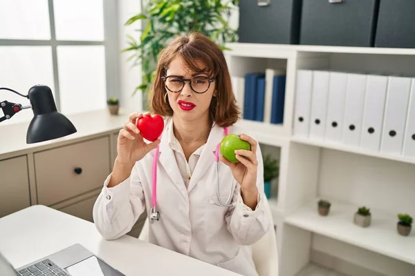 Mujer Doctora Joven Sosteniendo Corazón Manzana Verde Expresión Despistada Confusa — Foto de Stock