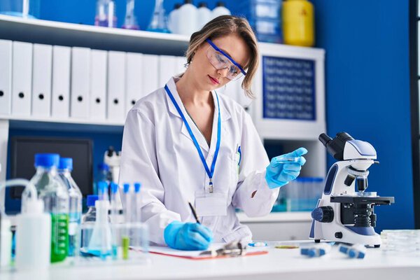 Young woman scientist writing report holding sample at laboratory