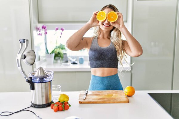 Young woman smiling confident holding orange over eyes at kitchen