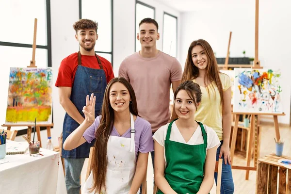 Group of five hispanic artists at art studio showing and pointing up with fingers number three while smiling confident and happy.