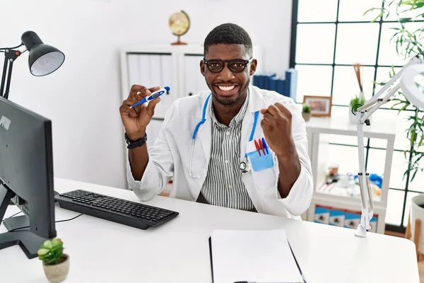 Young african american doctor man wearing doctor uniform holding thermometer at the clinic screaming proud, celebrating victory and success very excited with raised arms
