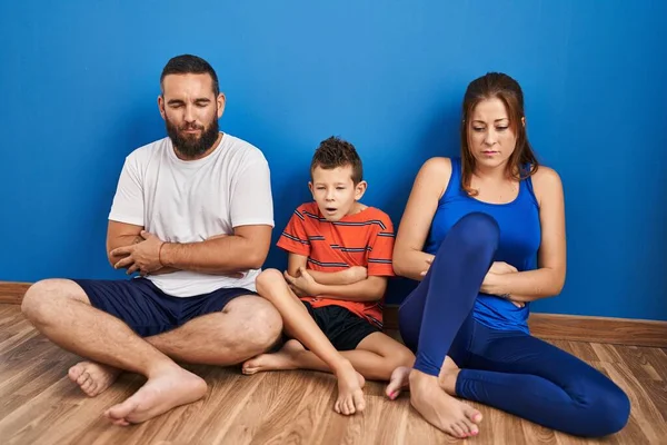 Family of three sitting on the floor at home with hand on stomach because nausea, painful disease feeling unwell. ache concept.