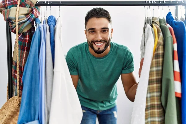Jovem Árabe Homem Cliente Sorrindo Confiante Aparecendo Através Rack Roupas — Fotografia de Stock